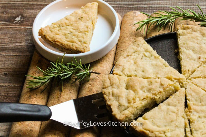 a single slice of shortbread rosemary slices. one slice is on a plate and four slices and one with a spatula underneath it