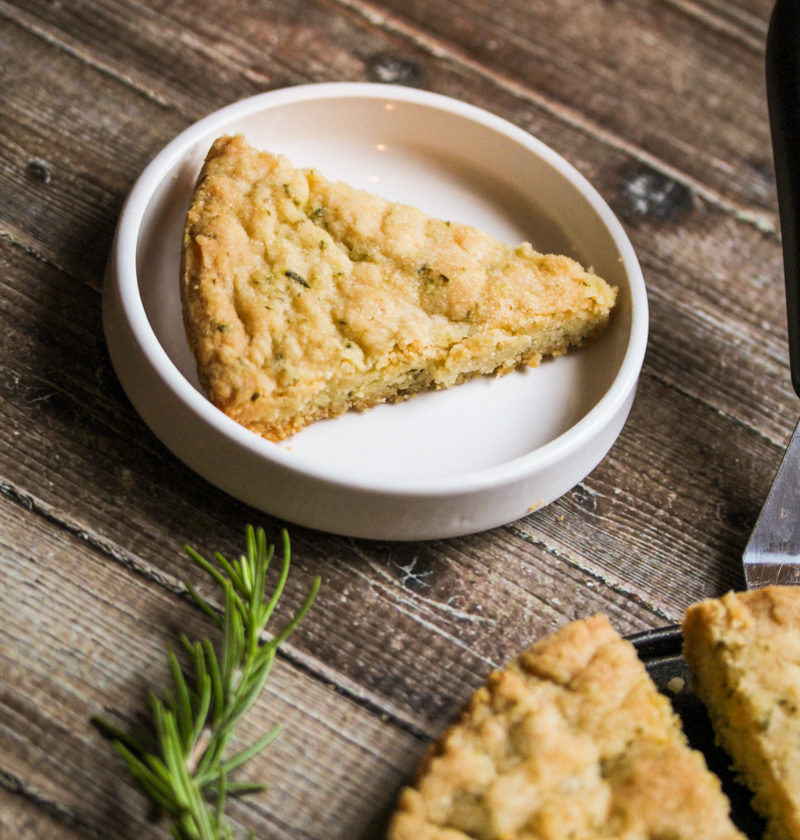 rosemary shortbread cookie slice on a white plate with a rosemary sprig in the foreground