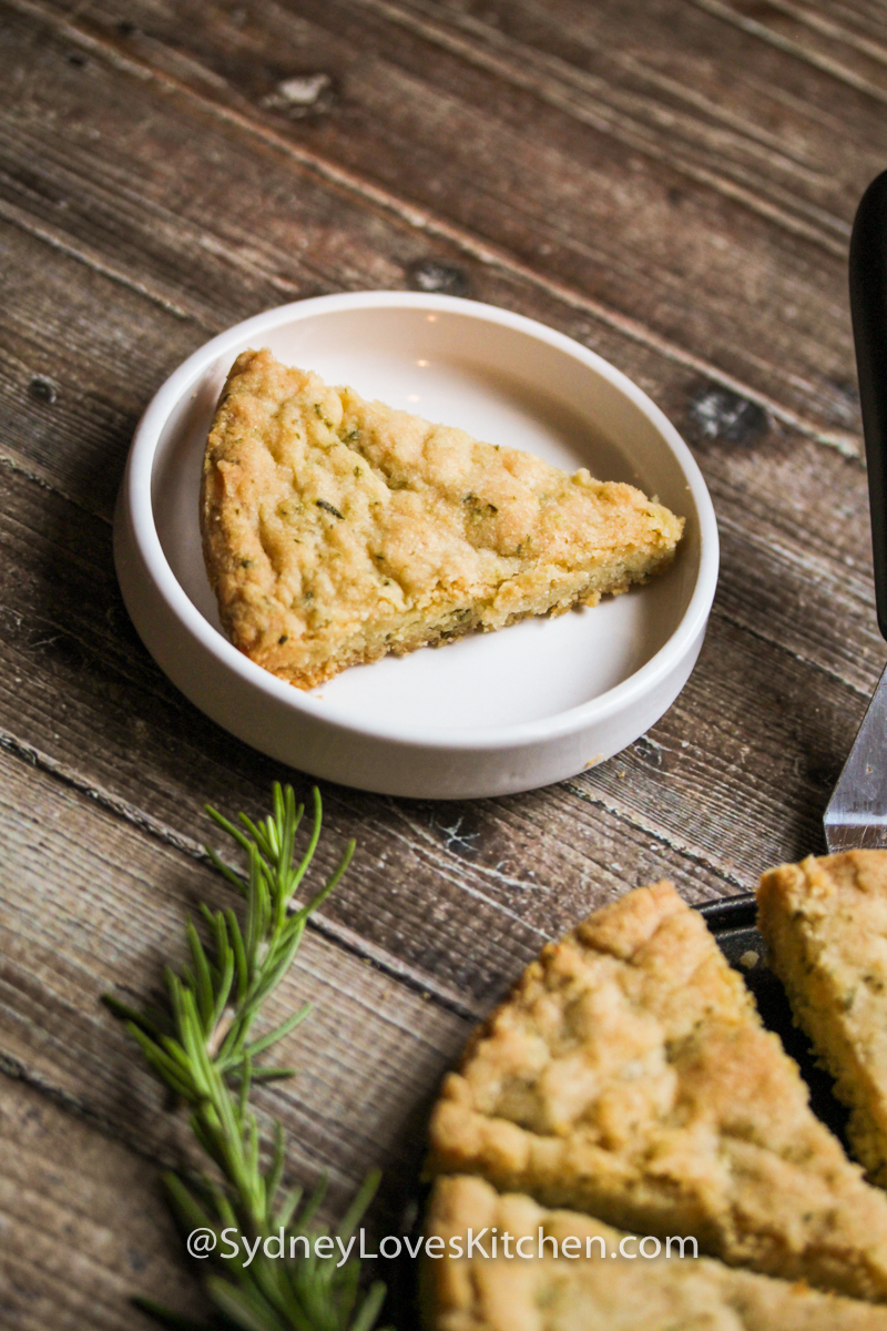 rosemary shortbread cookie slice on a white plate with a rosemary sprig in the foreground