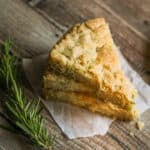 three slices of rosemary shortbread cookies stacked on top of each other with a sprig of rosemary in the foreground