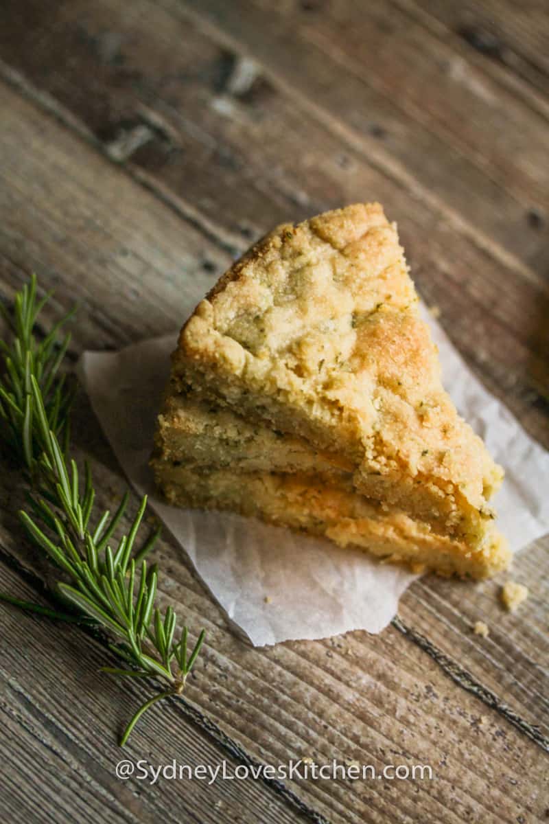 three slices of rosemary shortbread cookies stacked on top of each other with a sprig of rosemary in the foreground