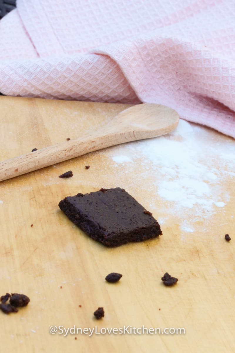 Easy Bake Oven Brownie with flour on the board, a wooden spoon and a pink towel in the background