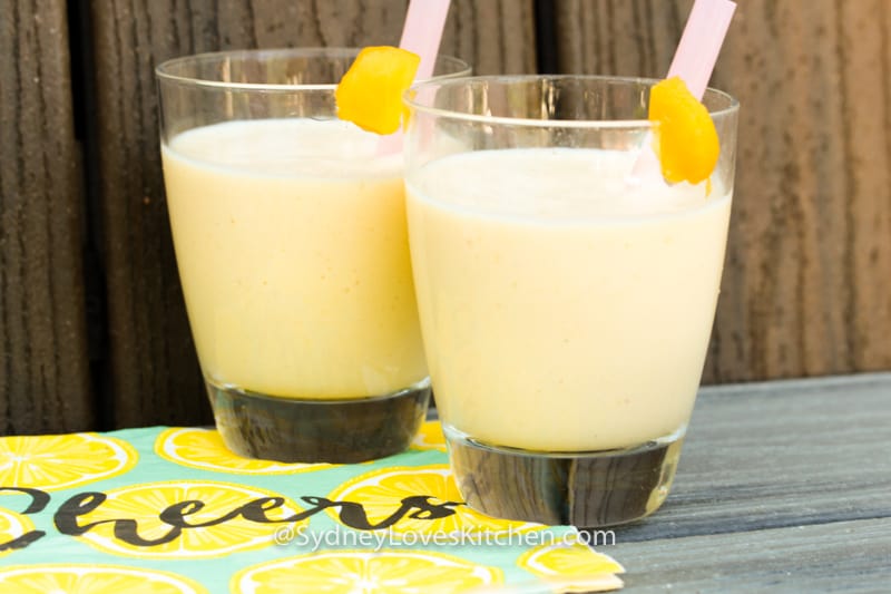 Two glasses of mango yogurt smoothies with a straw in each glass and a wedge of mango on the edge of each glass.