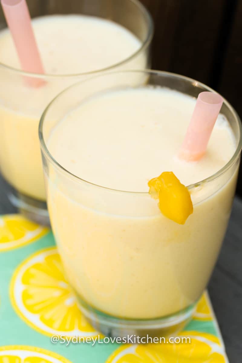 two glasses of mango yogurt with pink straws in each glass.