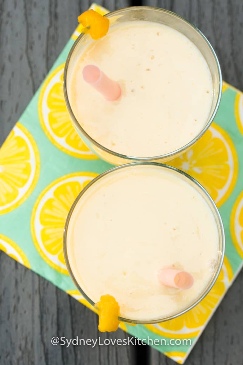 An overhead view of two glasses of mango yogurt smoothie with a napkin underneath.