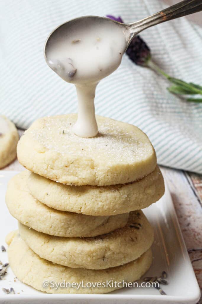 Stack of 4 Lavender cookies with lemon frosting poured on the stack on a white plate