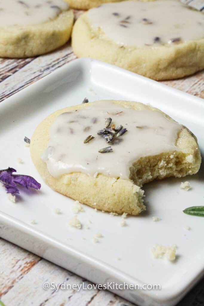 Lavender cookie with lemon frosting on a white plate with a bite taken from it.