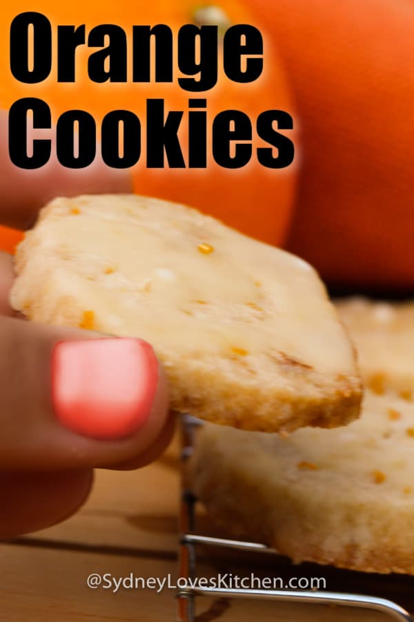 hand holding an orange cookie with two cookies in the background and oranges